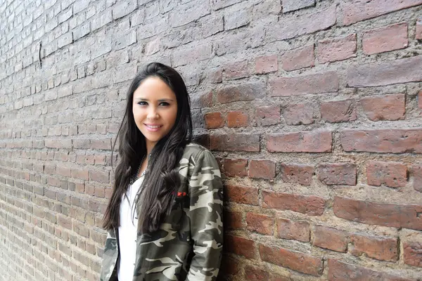 Hispanic woman against a brick wall.