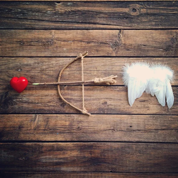 Bow with arrow, red heart and angel wings on a wooden background