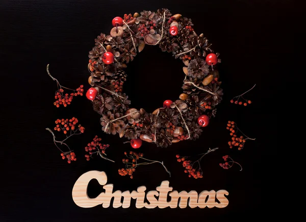 Christmas wreath and christmas wooden writing on black.