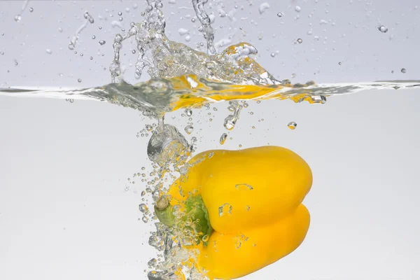 Close up view of a falling into water bright fresh yellow paprika with splashes and bubbles.