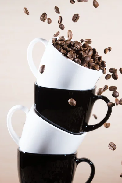 Close up of white and black cups on the stack with falling down brown roasted coffee beans.