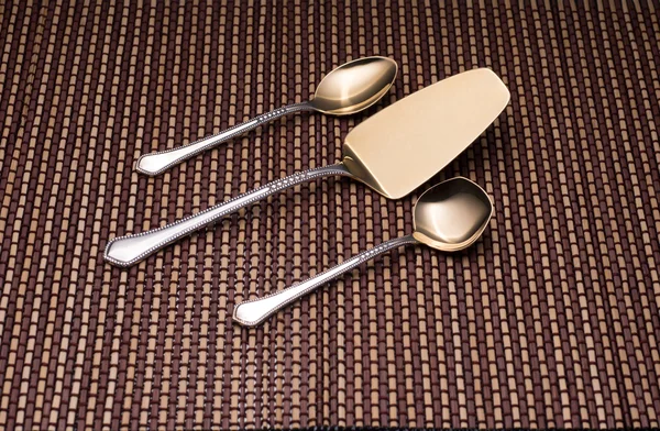 Classic silver kitchen utensils for dessert. Teaspoon, shovel cake and spoon for sugar on pattern table mat.