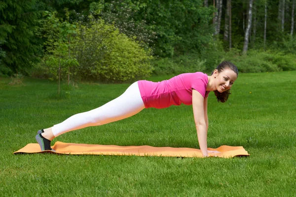 Woman keeping body in plank parallel to ground with straight hands on mat.