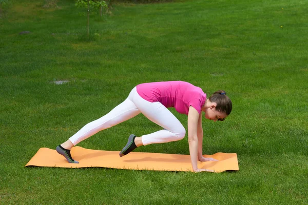 Brown haired woman training stomach, back, arms and legs muscles in plank on mat.