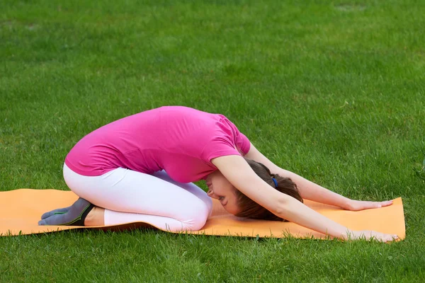 Beautiful brown haired woman with closed eyes doing stretching of the back during exercises in sitting pose.