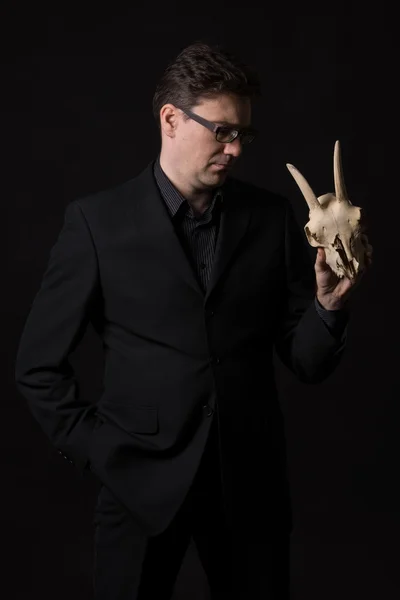 Pensive man wearing a black suit holding in one hand an animal skull