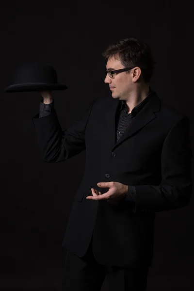 Man wearing a black suit holding a bowler hat in one hand