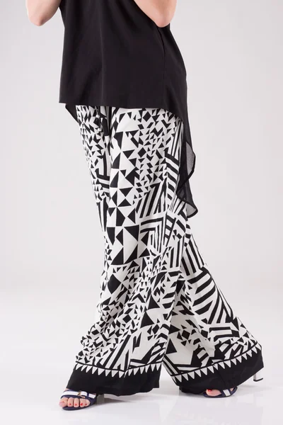 Feminine costume black blouse with a long back and wide black and white trousers with pattern.