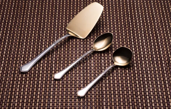 Silver kitchen utensils with golden spraying at the end. Shovel cake, teaspoon and spoon for sugar.