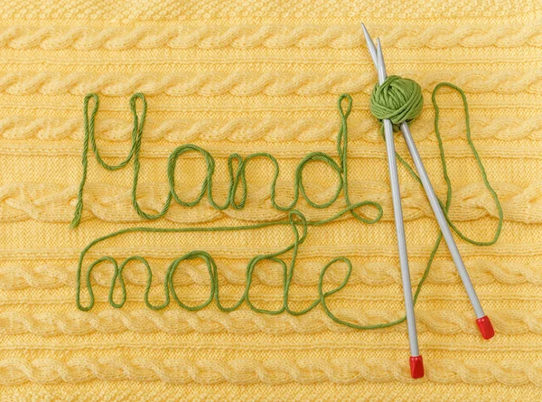 Yellow Knitted Background with Pattern and Braids;Grey Knitting Needle and Green Ball.Hand Made;Fancywork.Sign Hand-made from Thread