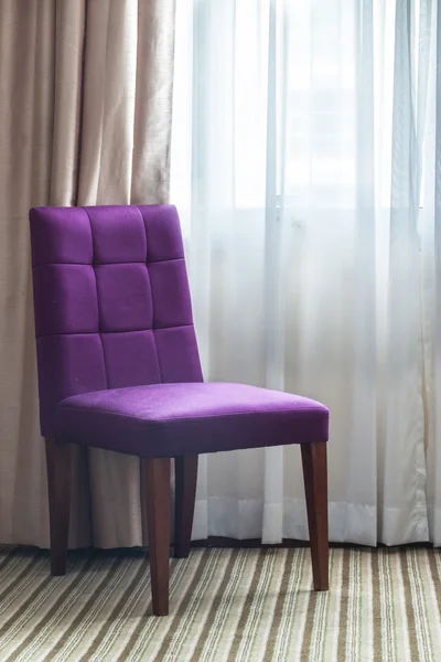Light shines through white curtains in room with purple chair