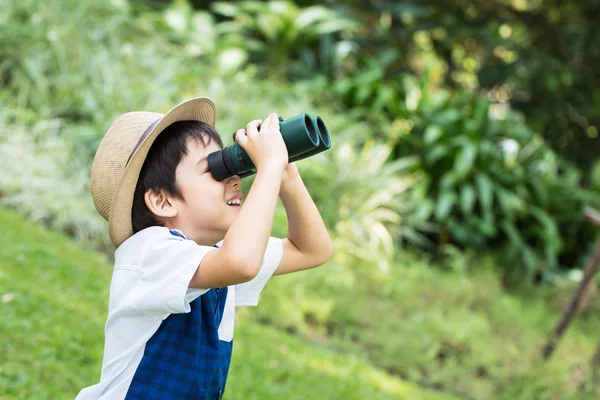 Little asian boy looking trough a binoculars with smiling face in park