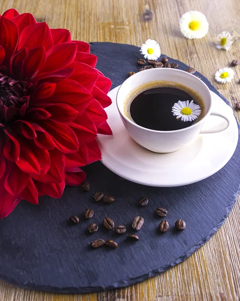 Composition made from cup of black tea with a black and brown background. Cup of black coffee with red flower, sugar, chamomile and coffee beans. It simbolizes nice morning with tasty tea.