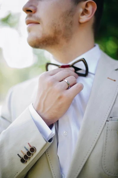 Groom straightens wooden bow tie on a suit