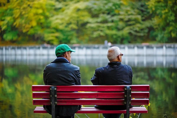 Two men sitting on bench at lake