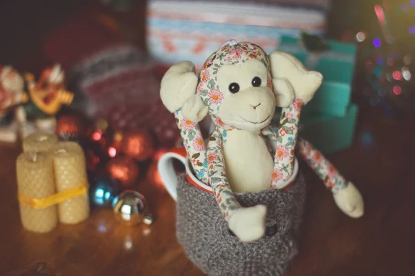 Knitted woolen cup with toy monkey on wooden table