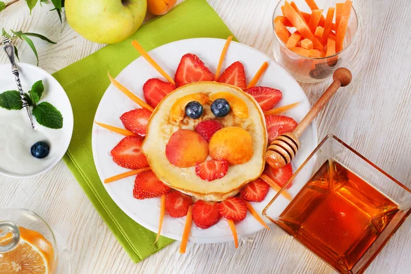 Childrens breakfast pancakes smiling face of the sun lion strawberry blueberry and apricot, cute food, honey