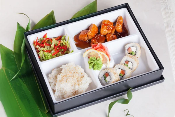 Sushi business lunch box, salmon teriyaki, roll sesame seeds, rice, wasabi, pickled ginger on top, bamboo leaves isolated, white background