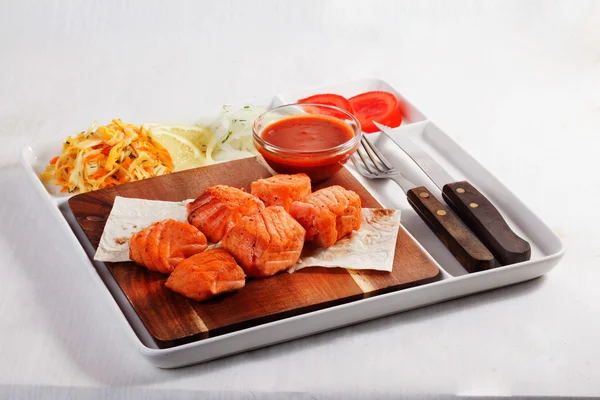 Skewers salmon with coleslaw, tomato, sauce on the board, paper, plate, fork, knife, isolated, menu