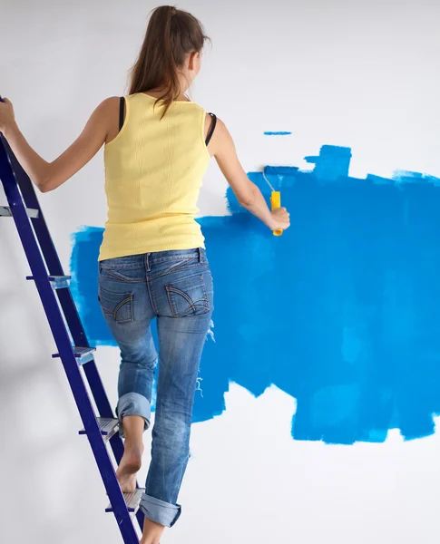Happy beautiful young woman doing wall painting, standing near ladder