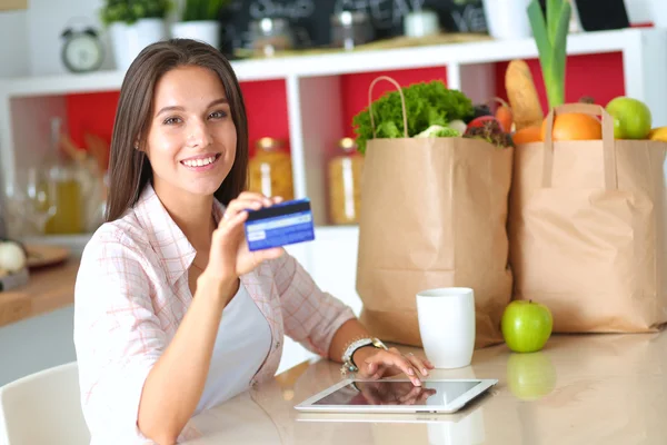 Smiling woman online shopping using tablet and credit card in kitchen