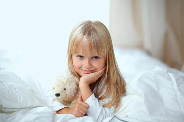 Little girl with teddy bear lying on the bed at home