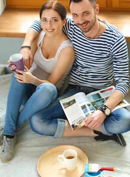 Attractive couple sitting on home floor looking at jurnal and smiling at each other.