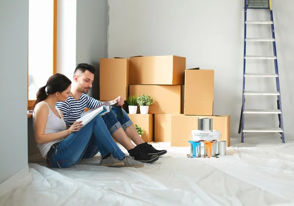 Attractive couple sitting on home floor looking at jurnal and smiling at each other.