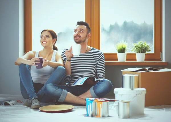 Attractive couple sitting on home floor looking at jurnal and smiling at each other.