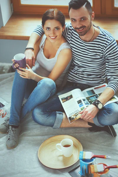 Attractive couple sitting on home floor looking at jurnal and smiling at each other.