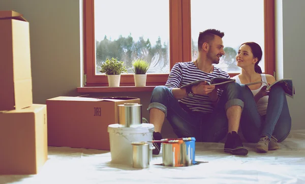 Attractive couple sitting on home floor looking at jurnal and smiling at each other.