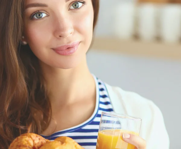 Young woman with glass of juice and cakes standing in kitchen .