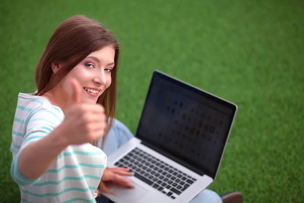 Young woman with laptop sitting on green grass