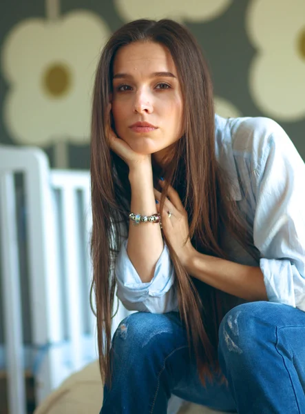 Young tired woman sitting on the bed near childrens cot.