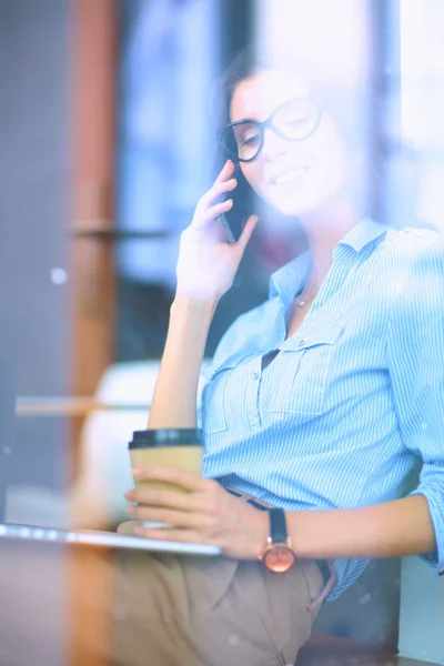 Beautiful young business woman sitting at office desk and talking on cell phone,