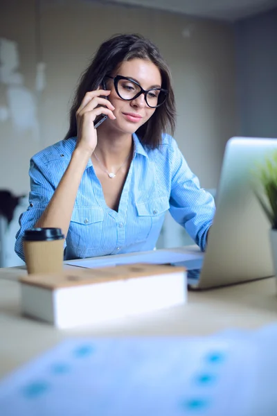 Beautiful young business woman sitting at office desk and talking on cell phone