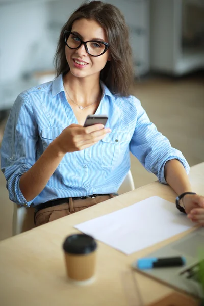 Beautiful young business woman sitting at office desk and talking on cell phone