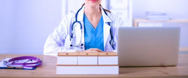 Beautiful young smiling female doctor sitting at the desk and writing.