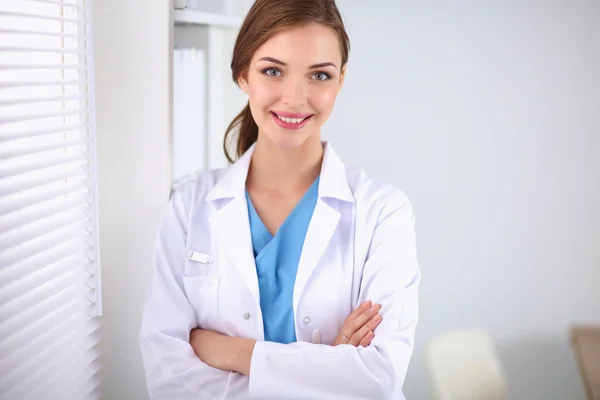 Woman doctor is standing near window with crossed arms
