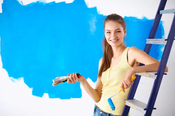 Happy beautiful young woman doing wall painting, sitting on ladder