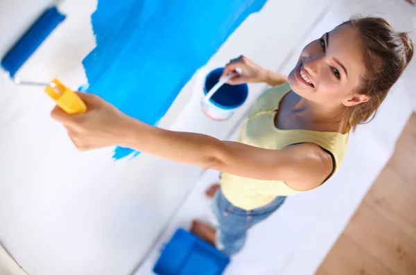 Happy beautiful young woman doing wall painting, standing on ladder