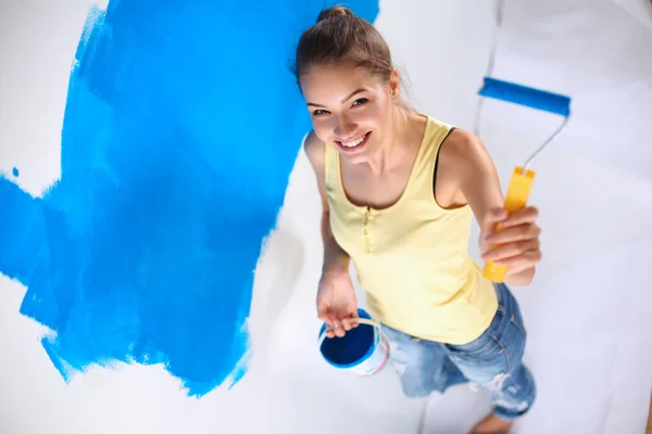 Happy beautiful young woman doing wall painting, standing on ladder