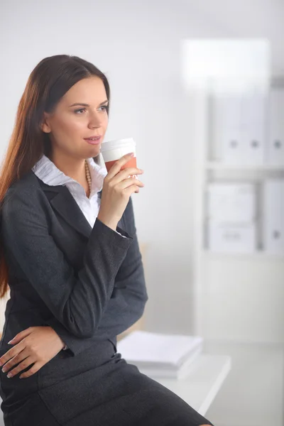 Woman drink coffee at office, standing near desk