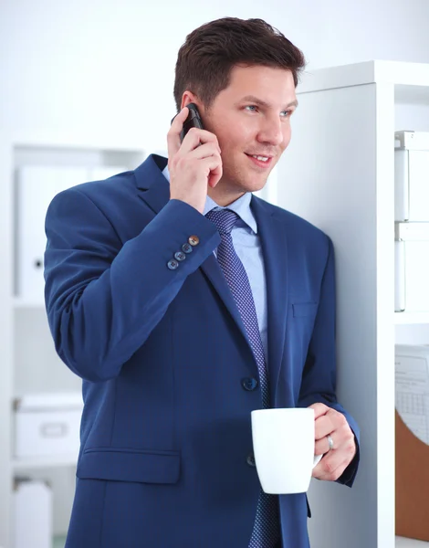 Smiling businessman standing and using mobile phone in office