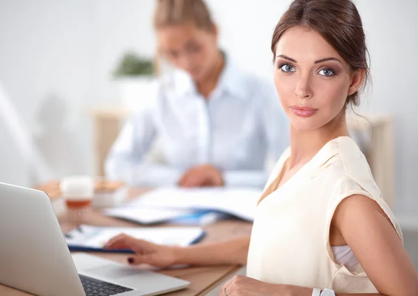 Two women working together at office, sitting on the desk