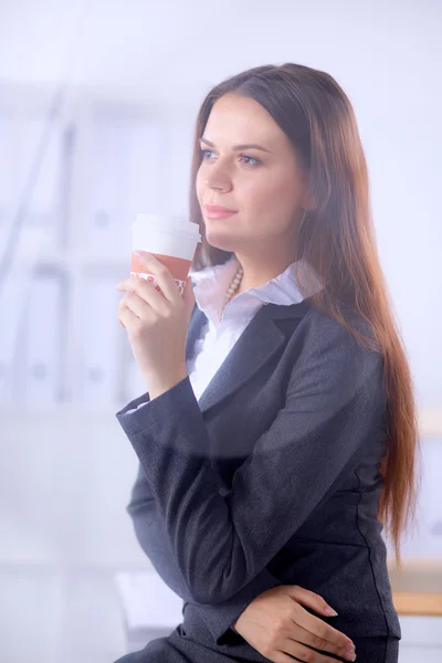 Woman drink coffee at office, standing near desk