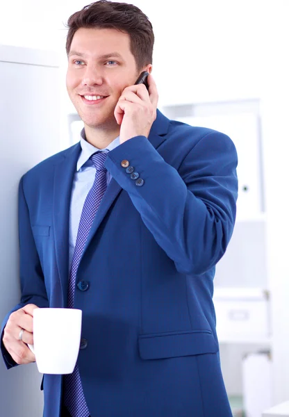 Smiling businessman standing and using mobile phone in office