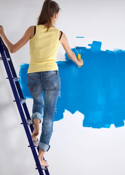 Happy beautiful young woman doing wall painting, standing near ladder