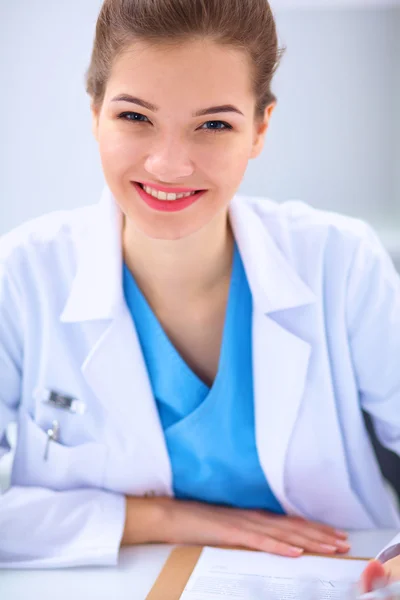 Beautiful young smiling female doctor sitting at the desk .