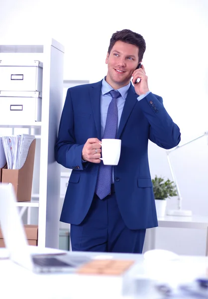 Smiling businessman standing and using mobile phone in office